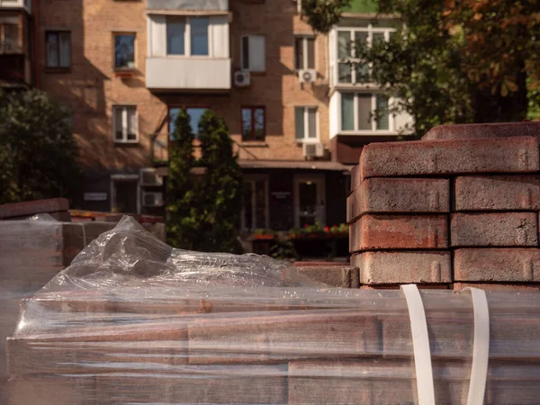 A stack of paving tiles and a pack of cigarettes in the foreground and and old red brick building lit by setting sun in the background in Kyiv, Ukraine. Road under construction concept.