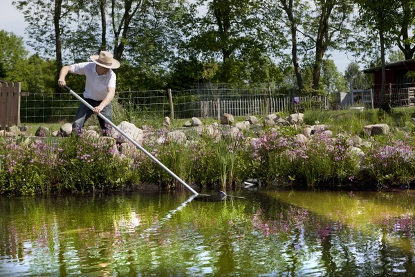 Gärtner mit Strohhut säubert Teich — Stockfoto