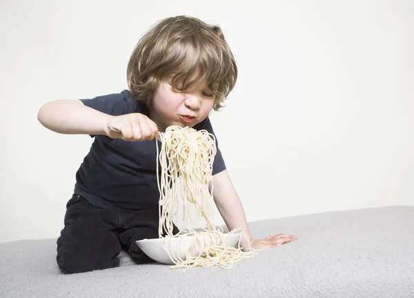 Dziecko jedzenie spaghetti na kanapie — Zdjęcie stockowe