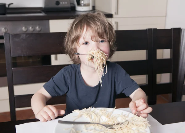 Chłopiec ma usta pełne makaronu w kuchni — Zdjęcie stockowe