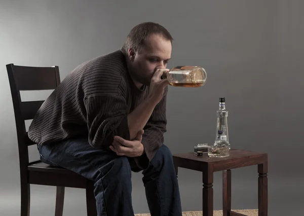 Депресивний молодий чоловік сидить на стільці, п'є пиво — стокове фото