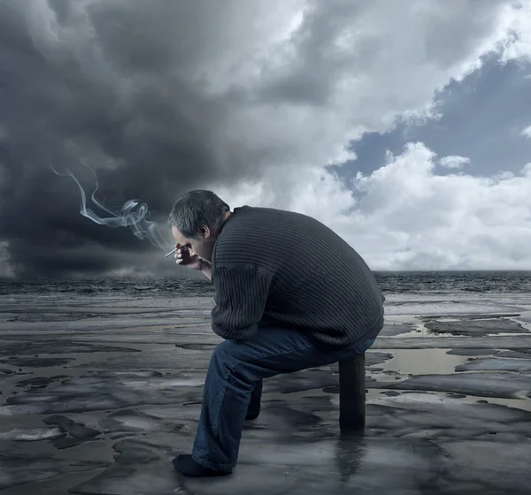 Depressed young man sitting on a chair, smoking a cigarette — Stock Photo, Image