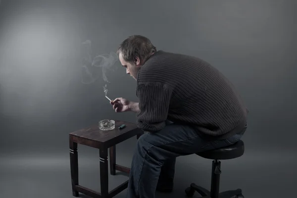 Depressed young man sitting on a chair, smoking a cigarette — Stock Photo, Image