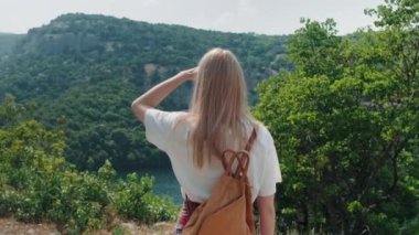 Kadın büyük manzaralı uçurum ve nehir manzarasına doğru yürüyor, el kamerasıyla çekilmiş..