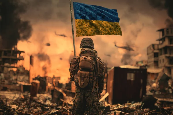 An Ukrainian soldier stands with a Ukrainian flag in his hand and looks at the ruined city