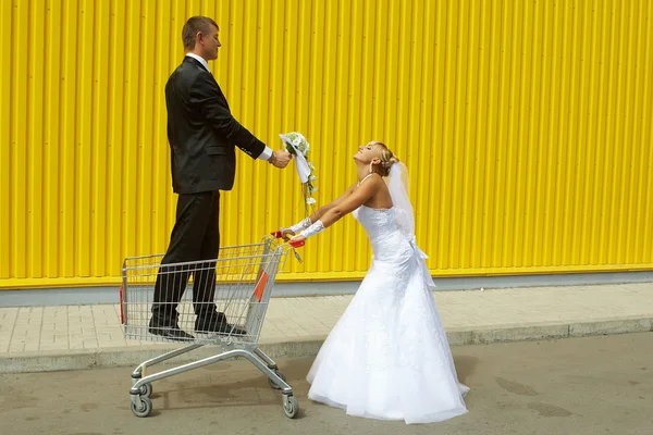 Noiva e noivo brincando com uma cesta de supermercado — Fotografia de Stock