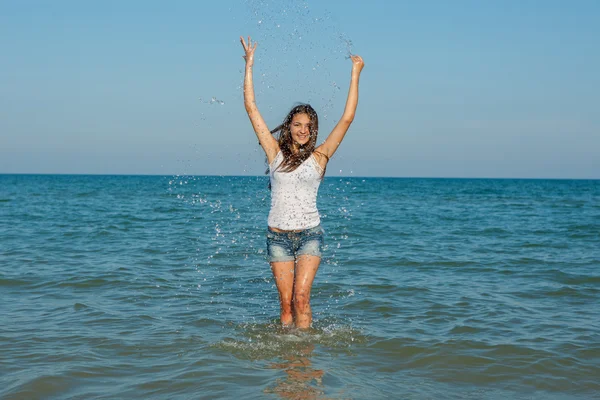 Молодая девушка плещущая воду в море — стоковое фото
