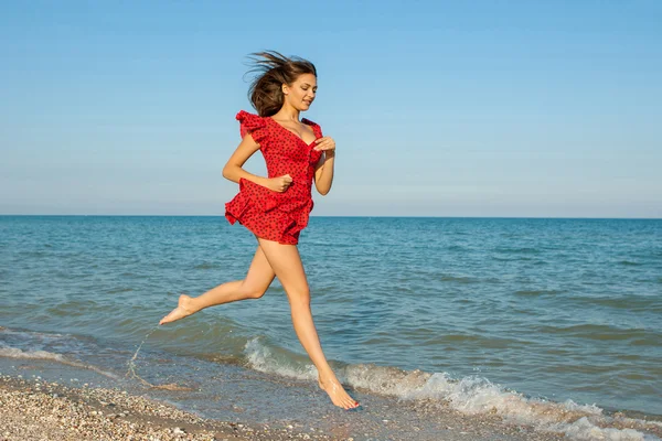 Young woman runs in red dress on the sea — Stock Photo, Image