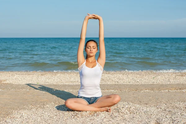 Mujer joven practicando yoga o fitness en la orilla del mar — Foto de Stock