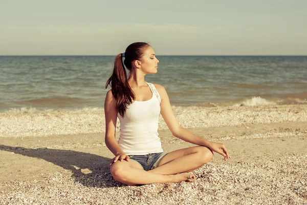 Mujer joven practicando yoga o fitness en la orilla del mar — Foto de Stock