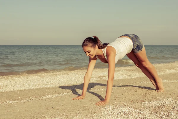 Mujer joven practicando yoga o fitness en la orilla del mar —  Fotos de Stock