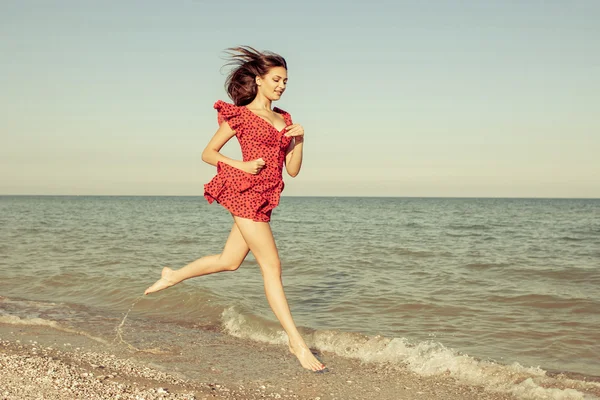 Genç kadın kırmızı elbise içinde deniz üzerinde çalışır. — Stok fotoğraf