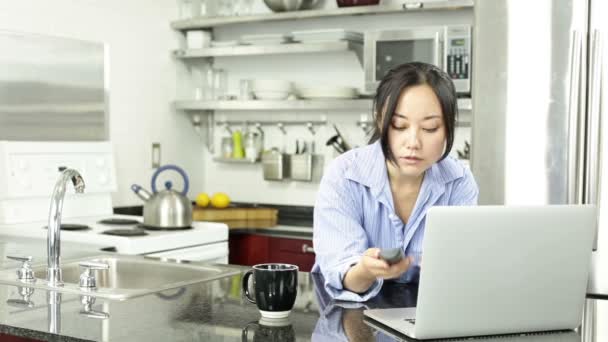 Asiática chica con un portátil en la cocina — Vídeos de Stock