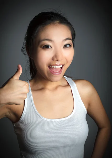 Attraente asiatico ragazza in un bianco t-shirt mostrando pollici fino — Foto Stock