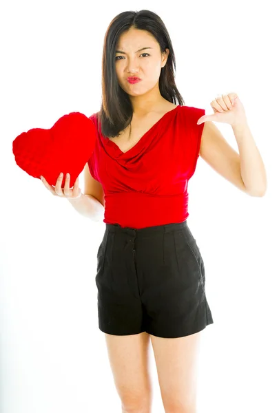 Woman holding heart shaped cushion and showing thumbs down — Stock Photo, Image