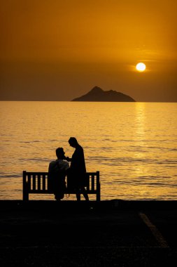 Güzel günbatımında deniz kenarında rahatlayan çiftlerin silueti.