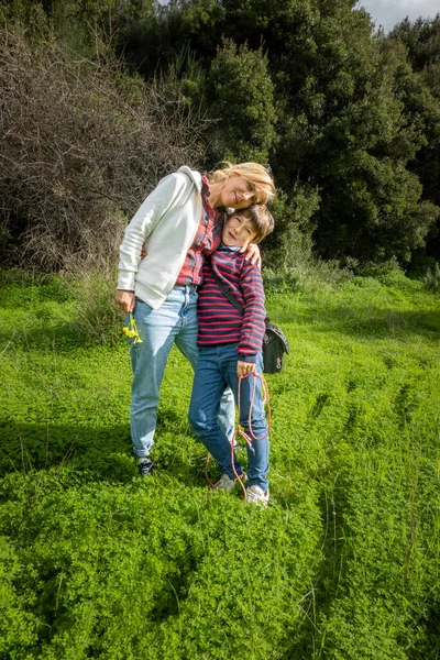 畑の緑の茂みの上に立って腕を持つ笑顔の母親と息子 — ストック写真