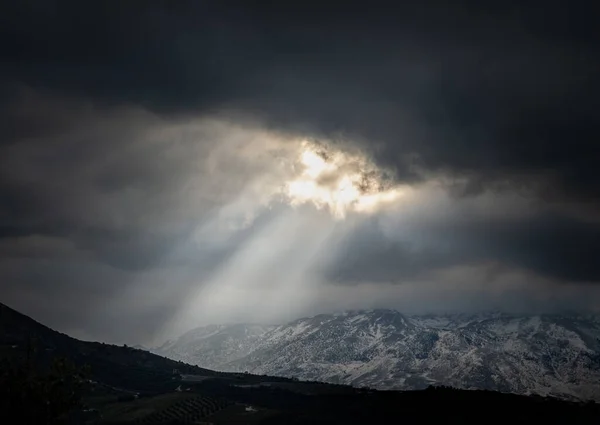 美丽的阳光从白雪覆盖的高山上的阴云中透射出来 — 图库照片