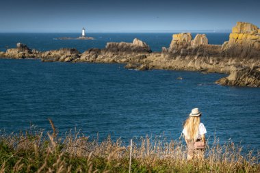 Rear view of woman in hat overlooking sea and cliff, Brittany, France clipart