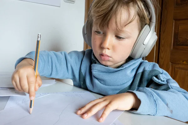 小男孩一边在家里用耳机听 一边在纸上画画 — 图库照片