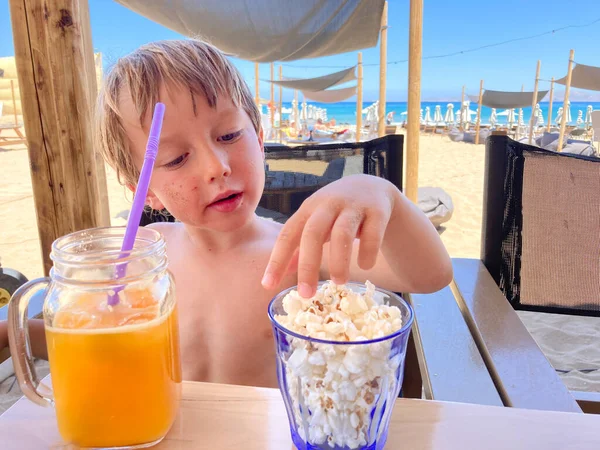 Niño Beber Jugo Comer Palomitas Maíz Mientras Relaja Playa —  Fotos de Stock