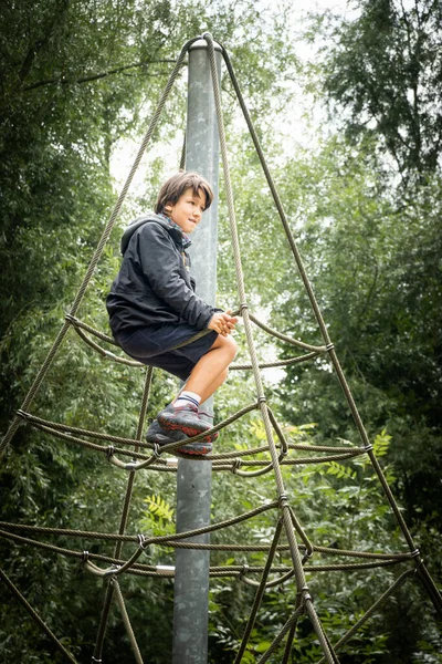 男孩坐在公园里攀爬架的顶部 — 图库照片
