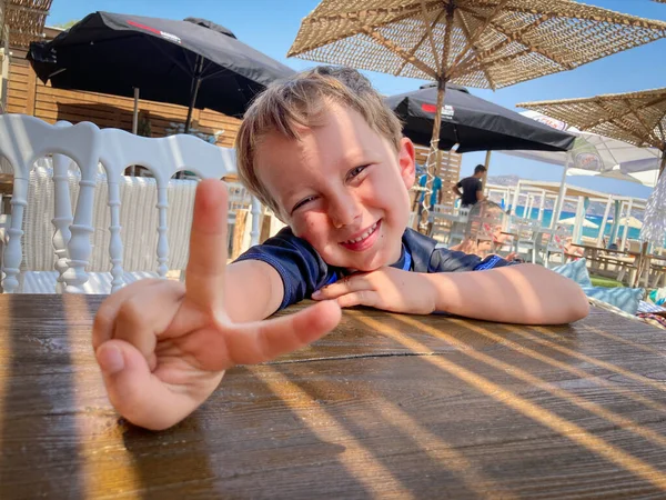 Muchacho Sonriente Mostrando Señal Paz Mientras Está Sentado Silla Mesa — Foto de Stock