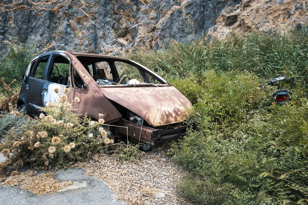 stock image Old broken car surrounded by bushes against rock formations