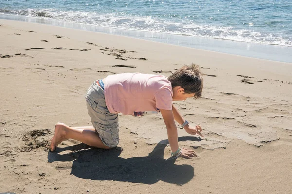 小男孩在海边的沙滩上画沙子 — 图库照片
