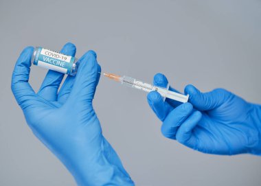 Covid-19 'a karşı aşı. Mavi eldivenli bir doktor elinde şırınga ve aşılı bir ampul tutuyor..
