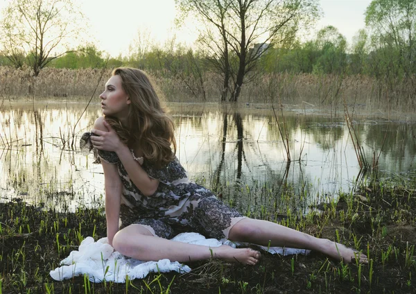 Retrato de la rubia de belleza sentada en el suelo con vestido en el fondo de la naturaleza Imagen De Stock
