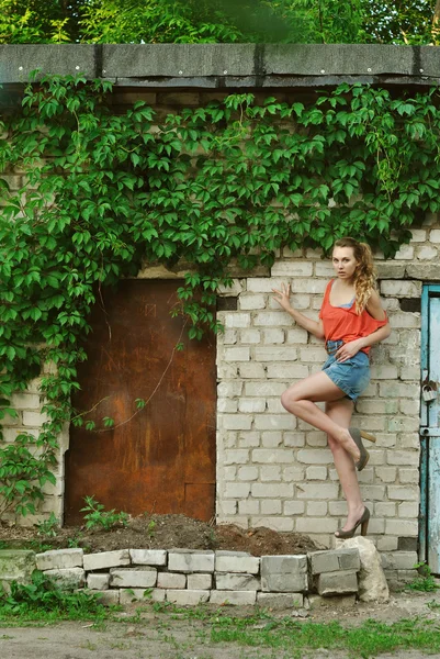 Retrato de menina de beleza de pé perto da parede de tijolo com uma perna para cima — Fotografia de Stock