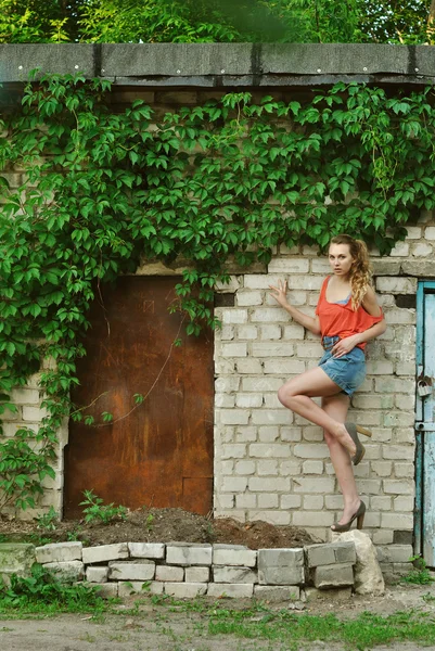 Retrato de chica de belleza de pie cerca de la pared de ladrillo con una pierna hacia arriba Imagen De Stock