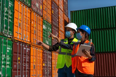 Lojistik mühendisi erkek ve kadın tıbbi maskeli ekip salgın sırasında büyük bir ticari rıhtımın önünde duruyor.