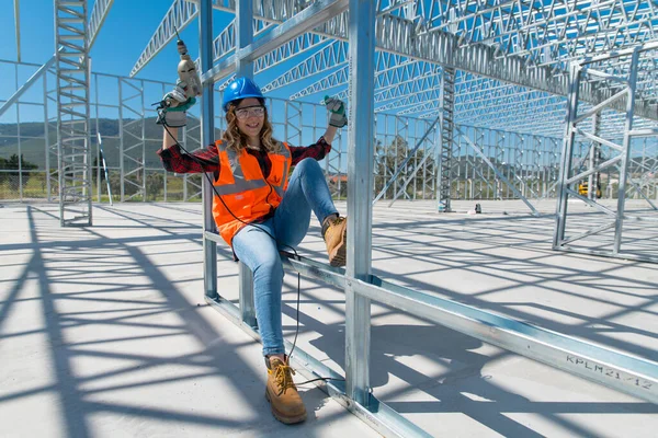 Cheerful construction worker smiling at the camera while sitting. Beautiful young woman, sitting in front of framework of the new building.