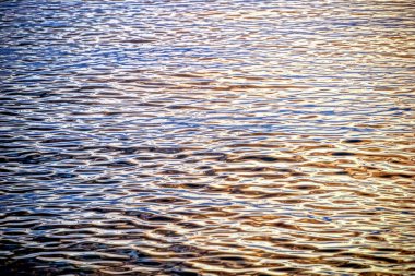 Dalgalı deniz suyu yüzeyinin soyut görüntüsü. Suyun üzerinde parlak güneş yansıması var.