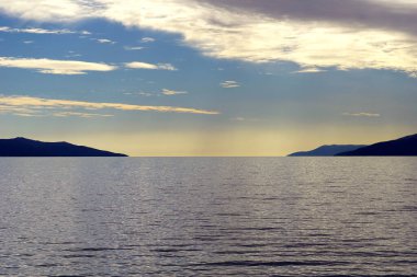 Fırtınadan sonra denizin üzerinde gün batımında iki ada silueti arasında bir deniz geçidi.