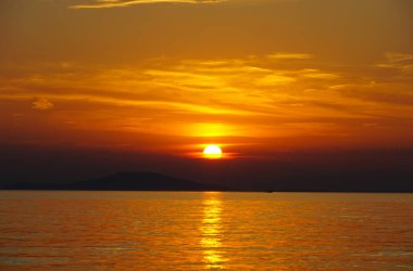 Global warming and Earth heating concept with yellow sun ball above dark clouds and orange sea surface