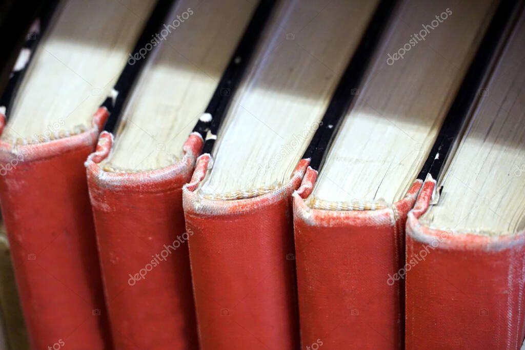 The spine of old, worn-out, red clothbound books on the bookshelves in the library