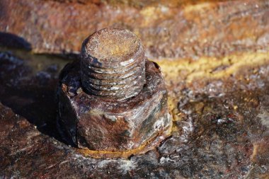 A damaged rusty screw with a nut on a rusty metal surface