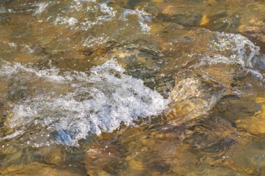 Güneşli bir dağ nehrinin desenli dalgaları