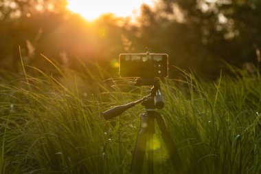 Akıllı telefon bir dağ nehrinde gün batımının videosunu çeker.