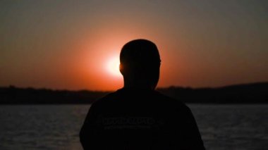 Silhouette of a mature man against the backdrop of a sunset on the lake