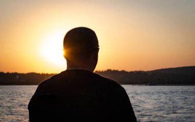 Silhouette of a mature man against the backdrop of a sunset on the lake