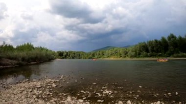 A group of people are floating on inflatable rafts in the distance along a mountain river
