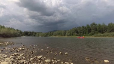 A group of people are floating on inflatable rafts in the distance along a mountain river