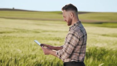 Çiftçi tarlanın yanında duruyor ve bir tabletle çalışıyor. O, sahaya bakıyor. Güneş ışıl ışıl parlıyor. Kamera onun etrafında hareket ediyor. 4K
