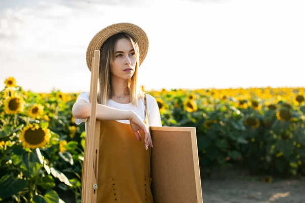 Gülümseyen bir kadının portresi. Ayçiçeklerinin arasında bir sehpanın yanında duruyor..