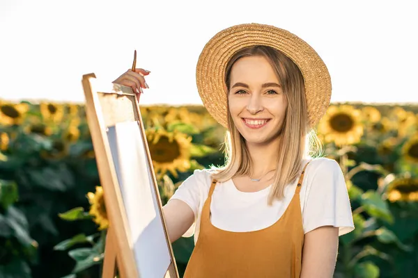 Gülümseyen bir kadının portresi. O, ayçiçeklerinin arasında bir sehpanın yanında duruyor. Kameraya bakıyor..
