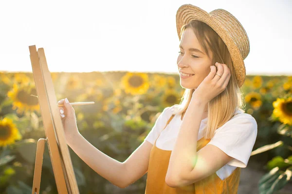 Ayçiçeği tarlasında duran ve resme bakan bir kadının portresi. Tuval bir sehpanın üzerinde duruyor. O gülümsüyor ve bir fırça tutuyor. Saçını düzeltiyor..